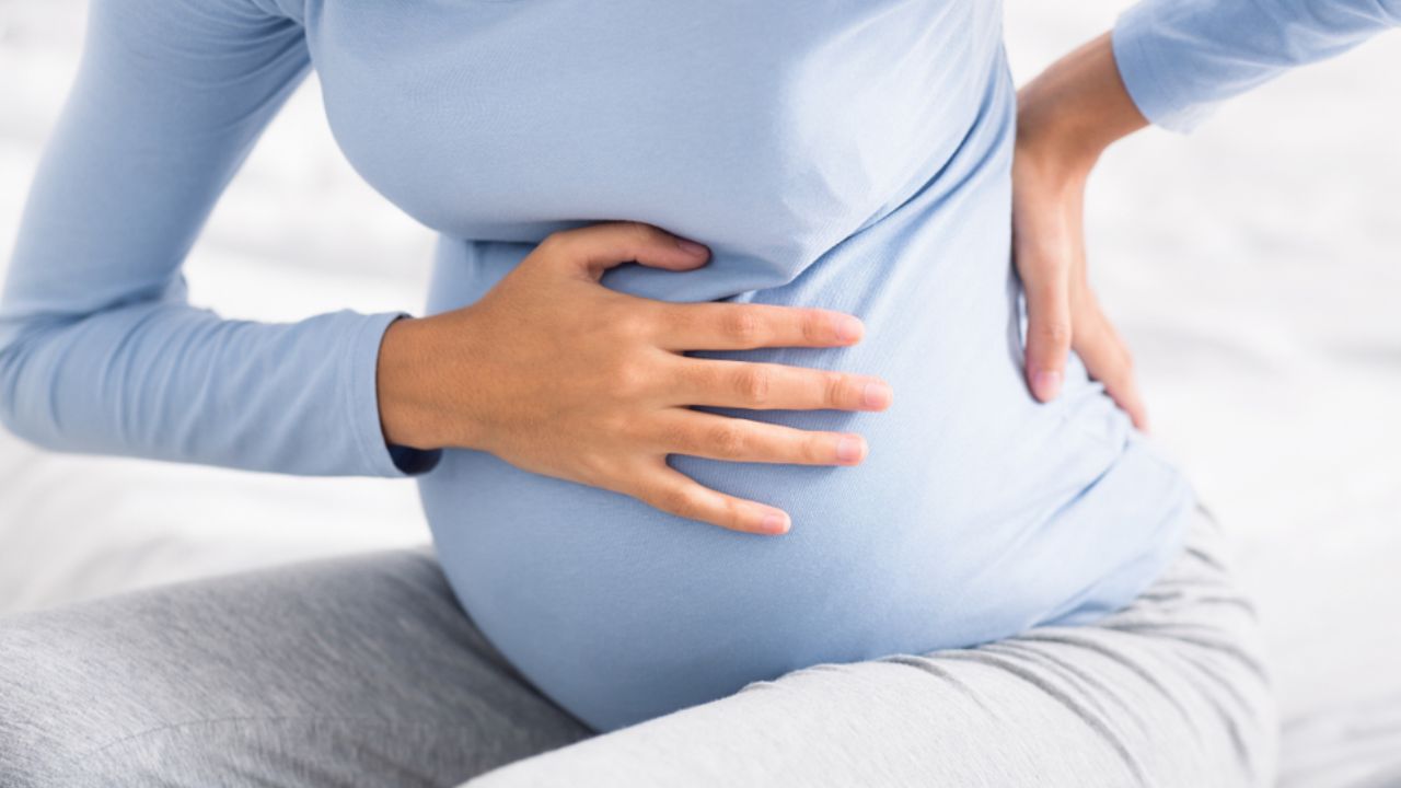 mulher grávida se apoiando na cama ao sentir cólica na gravidez