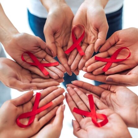 Mãos segurando fita vermelha, símbolo do Dezembro Vermelho