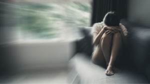 Uma moça sentada no sofá, com a cabeça apoiada das pernas, sofrendo de transtorno misto ansioso e depressivo.