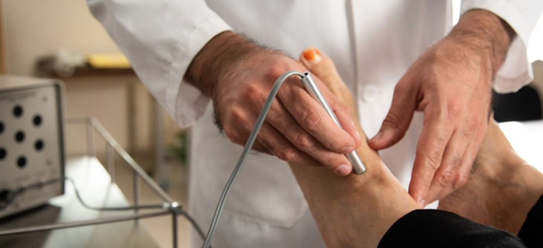 Angiologista realizando procedimento em pé de paciente.