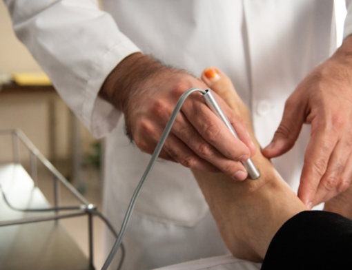 Angiologista realizando procedimento em pé de paciente.