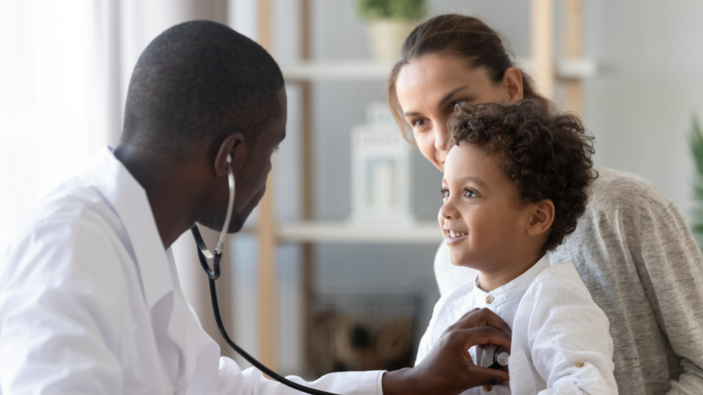 Um médico pediatra escutando os batimentos cardíacos de criança no colo da mãe.