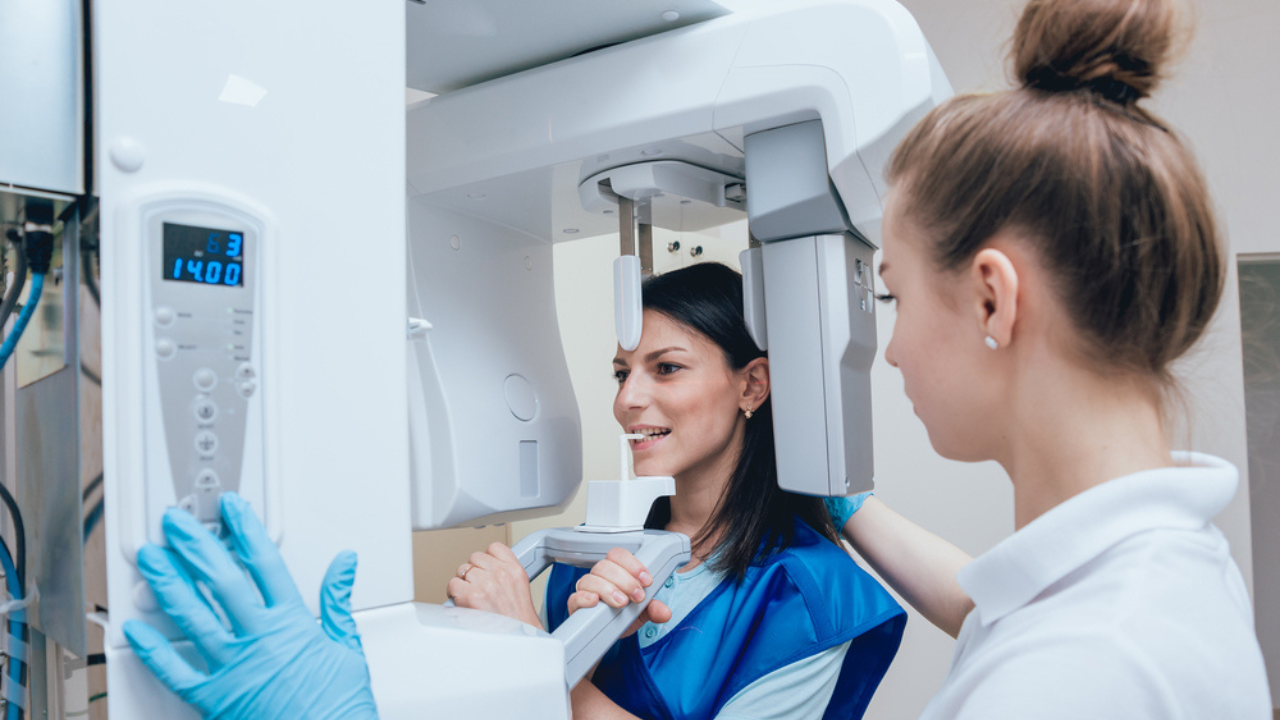 Médica posicionando paciente para iniciar o exame de raio X panorâmico dos dentes.