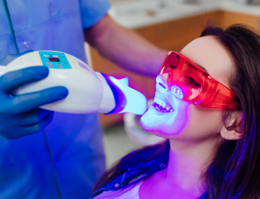 Um dentista realizando aplicação de clareamento dental a laser em uma paciente no consultório odontológico.