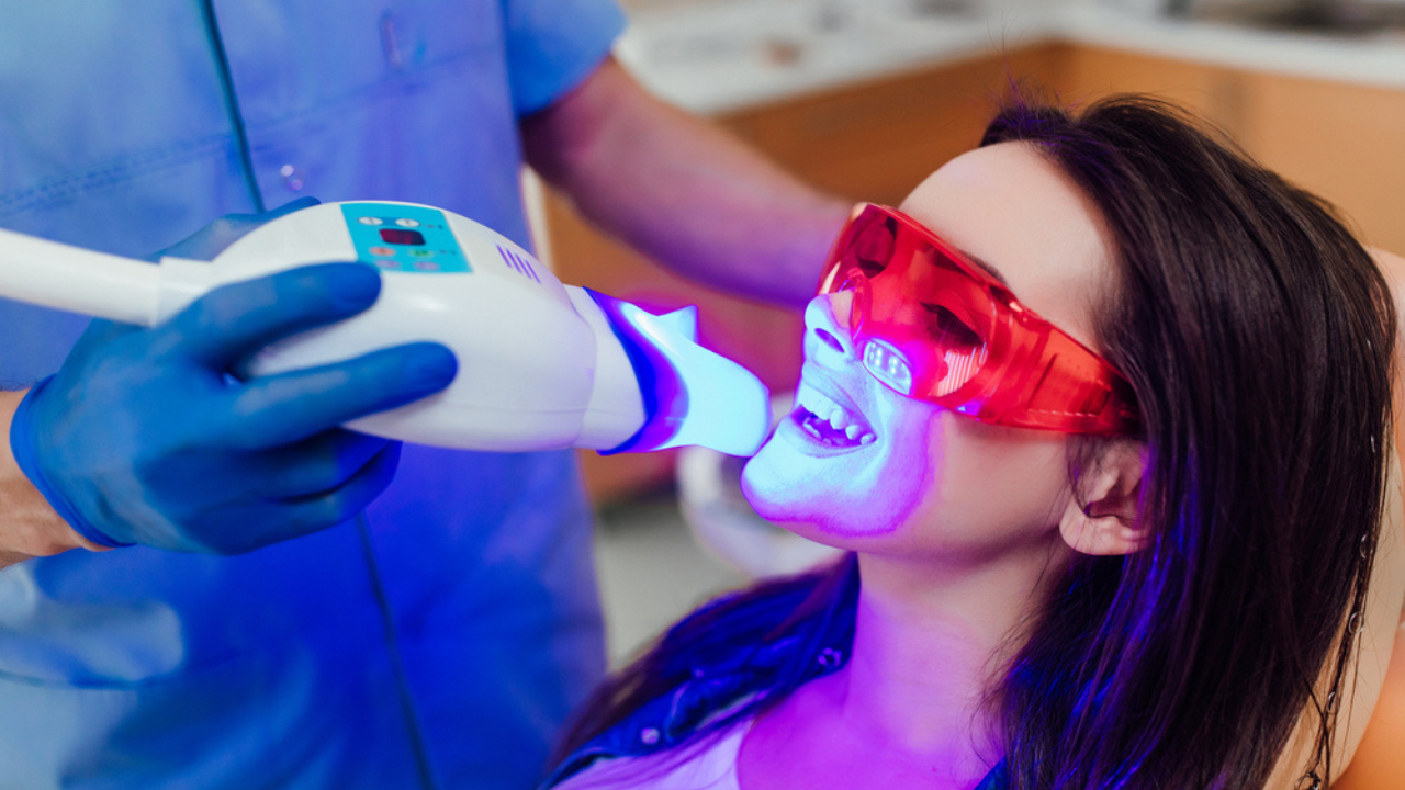 Um dentista realizando aplicação de clareamento dental a laser em uma paciente no consultório odontológico.