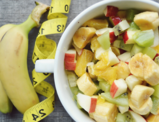 Uma tigela de salada de frutas com fita métrica ao lado. / qual a diferença entre nutricionista e nutrologo