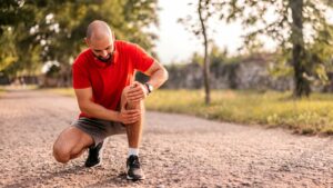 Homem se agachando para colocar as mãos no joelho esquerdo