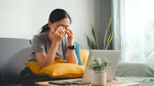 Mulher sentada em sofá com mãos sobre olhos por conta do desconforto causado pela conjuntivite